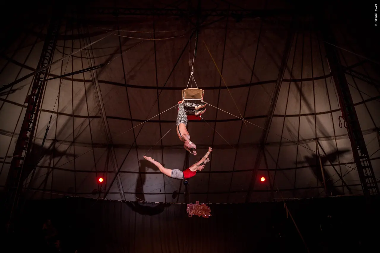 Dupla de trapezistas no alto da lona do circo, iluminada de vermelho