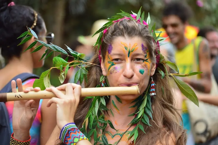 Artista com o rosto pintado e coroa de folhas toca flauta